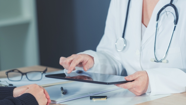 Doctor holding computer tablet while talking with a patient.