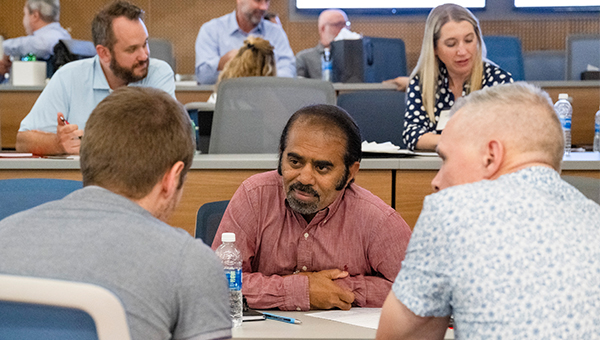 Man leans forward over desk to listen to a colleague.