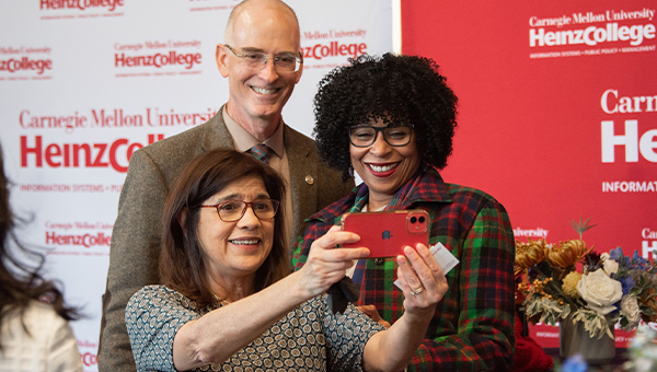 A woman takes a selfie with two friends at a Heinz College social event.