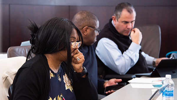 Three people sit at a desk listening to the presentation.