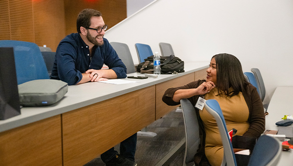 A man and woman sit in a classroom chatting between sessions.