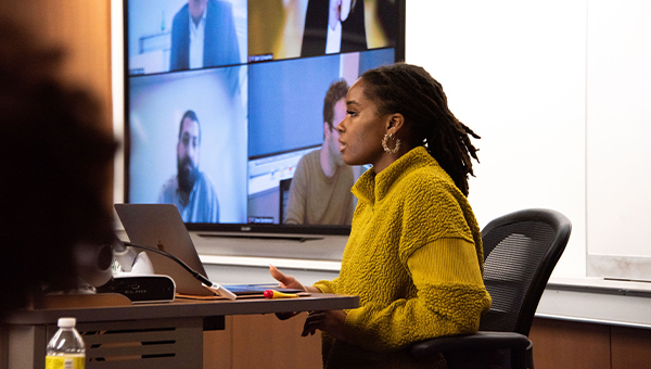 Woman in yellow sweater moderates discussion from the front of a classroom.