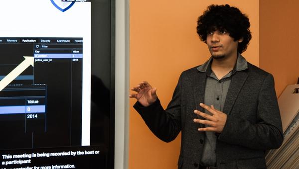 Student standing in front of a digital display presents capstone report findings.