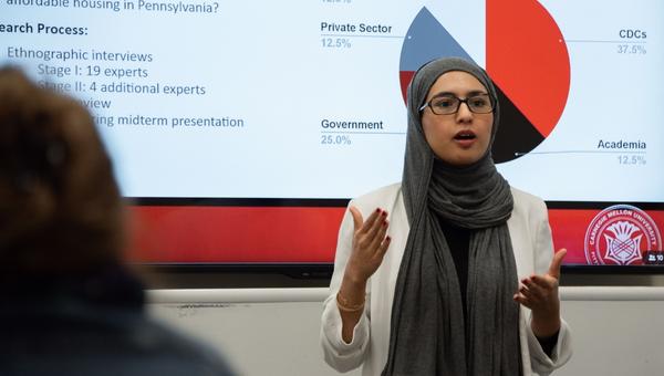 Student wearing a headscarf presents her capstone report findings.