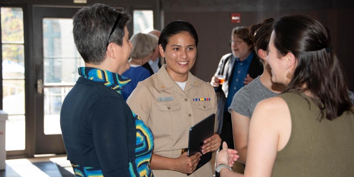 Member of the military in uniform chatting with two guests at a reception in the Heinz College rotunda