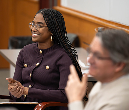 A student sits next to a professor at the front of the classroom.