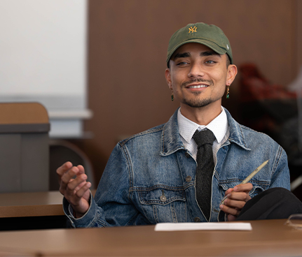 A student in a hat and denim jacket smiles.